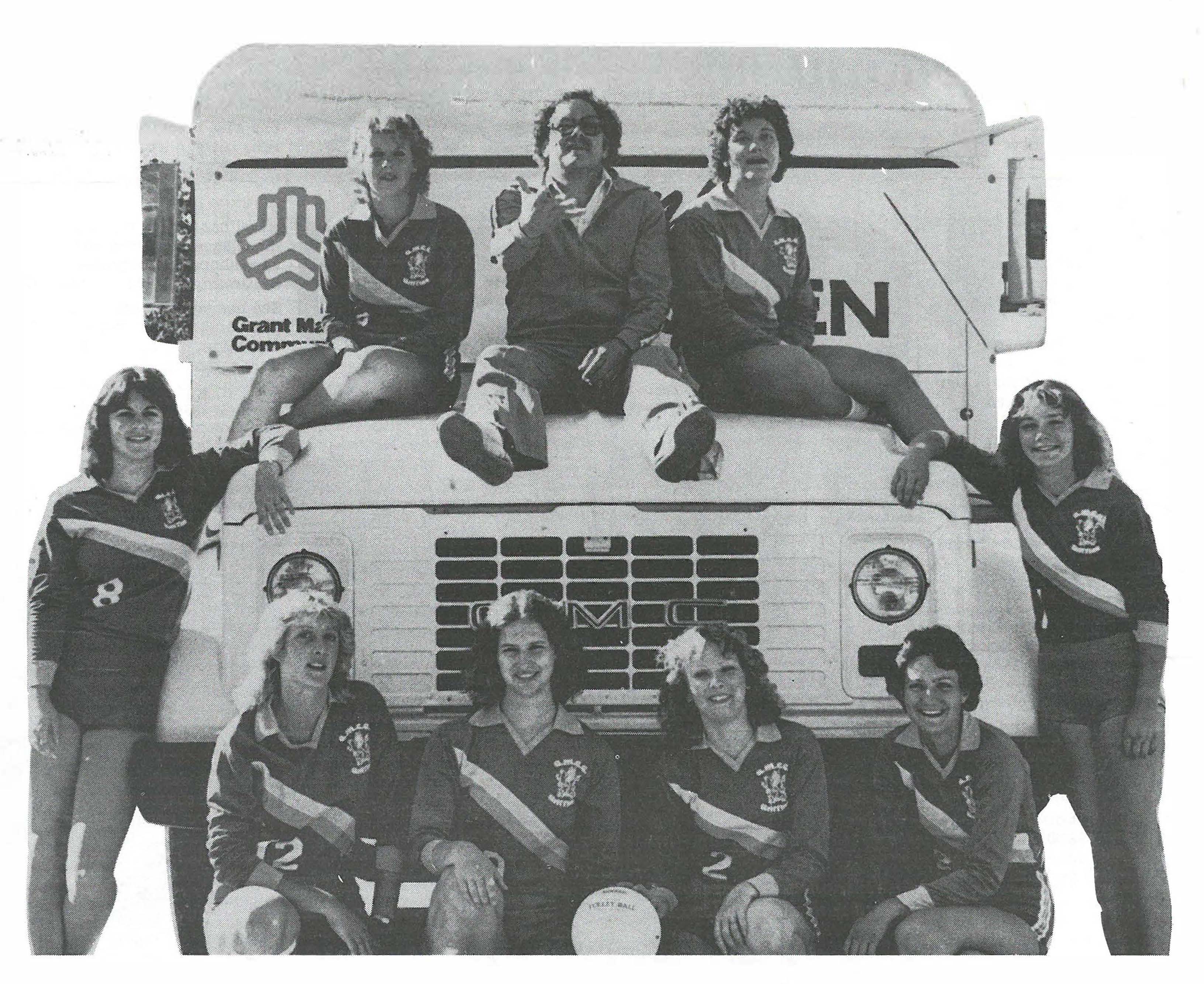 Photograph of the women's volleyball team from 1981 and their coach sitting on top of and around a bus.
