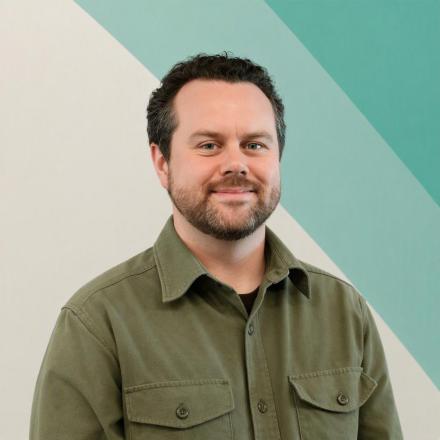 Image of a white man in a green shirt against a cream and green background.